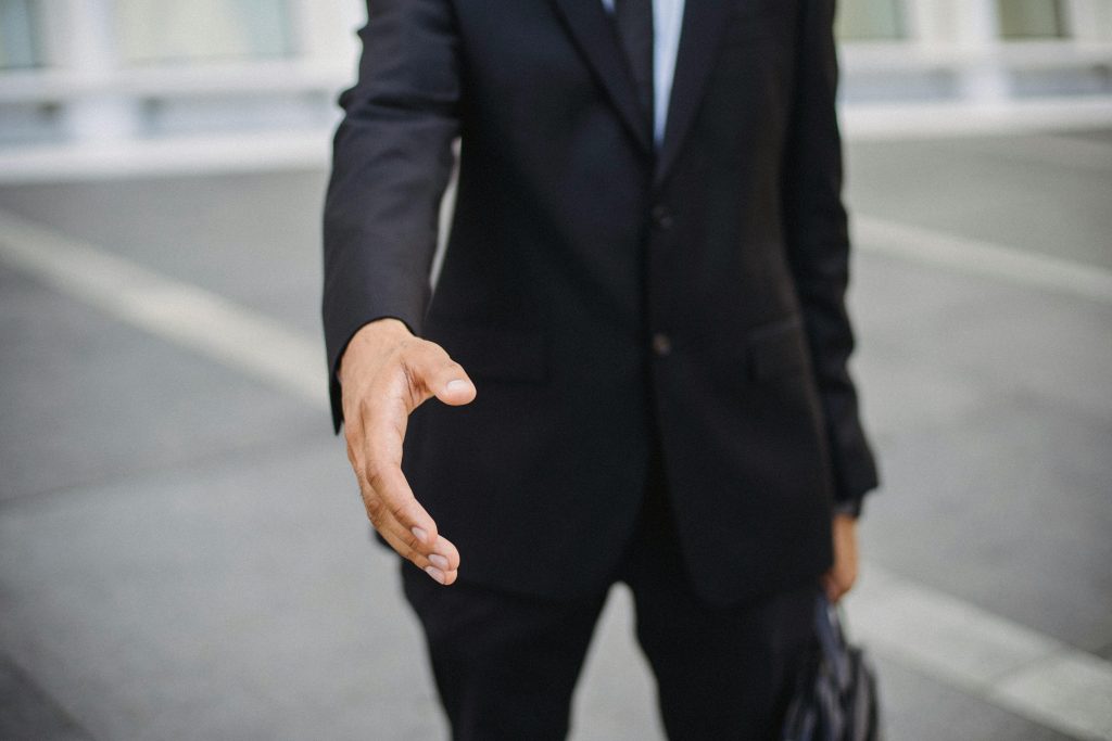 pexels photo 4965006 4965006 Close-up of a businessman in a suit reaching out for a handshake, symbolizing connection.