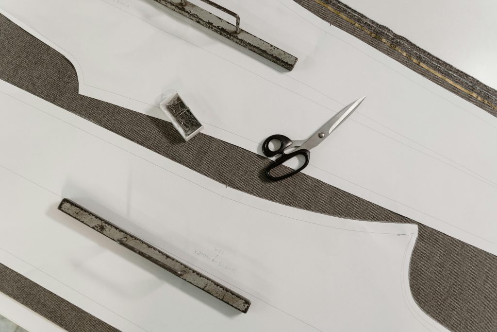 Detailed view of scissors, pattern paper, and fabric on a tailor's workbench.